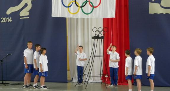 chłopcy w strojach sportowych stoją pod flagą igrzysk olimpijskich na sali gimnastycznej podczas ceremonii