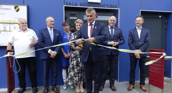 mężczyzna w towarzystwie grupy osób przecina wstęgę z okazji otwarcia nowego budynku klubowego MGKS Drzewica