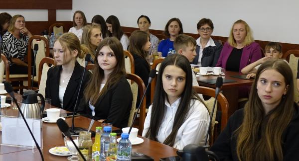 Uczestnicy sesji siedzą przy stołach w sali konferencyjnej Urzędu Miejskiego w Drzewicy. W centrum zdjęcia młodzieżowe radne, z tyłu m.in. nauczycielki.