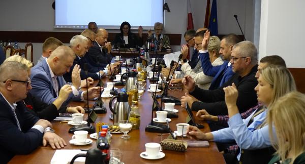 Uczestnicy sesji siedzą przy stołach w sali konferencyjnej Urzędu Miejskiego w Drzewicy. Radni biorą udział w głosowaniu