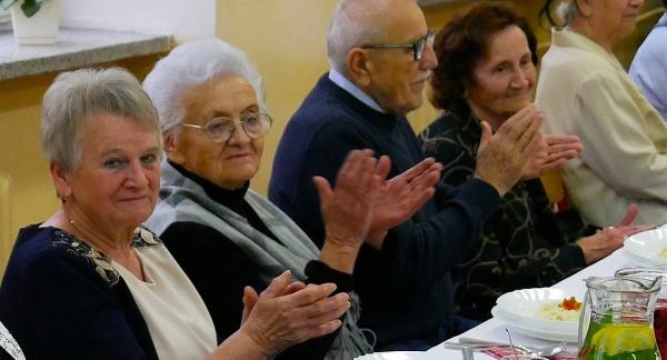 Pięcioro emerytowanych nauczycieli siedzi przy stole. Pięć osób klaszcze.