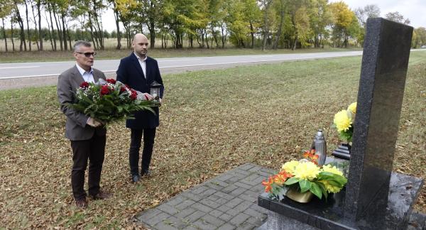 Pomnik nagrobny, po lewej stoją Burmistrz Drzewicy Janusz Reszelewski trzymający wieniec i Zastępca Burmistrza Drzewicy Dominik Niemirski trzymający znicz. W tle pas drogi wojewódzkiej. 
