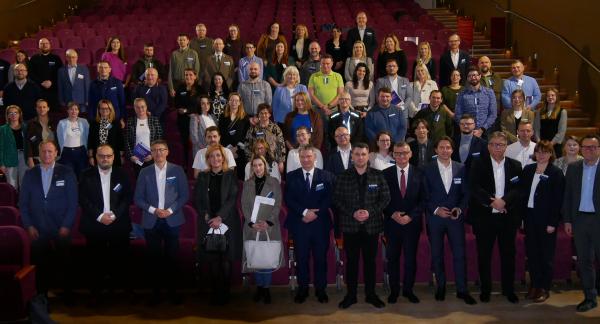 Wspólne zdjęcie uczestników spotkania stojących w rzędach na widowni sali kinowo-widowiskowej RCK