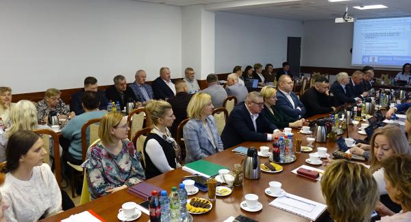 Kilkadziesiąt osób uczestniczących w sesji siedzi przy stołach w sali konferencyjnej Urzędu Miejskiego w Drzewicy. Widok ogólny z góry.