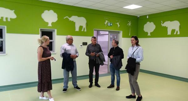 Grupa pięciu osób rozmawia w dużej, jasnej sali z zielonymi dekoracjami ściennymi przedstawiającymi zwierzęta.