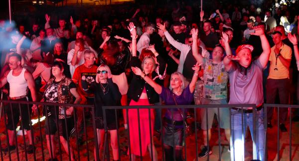 Tłum ludzi bawiący się i tańczący przy barierce pod sceną na plenerowym festiwalu w Drzewicy. Widok nocny.