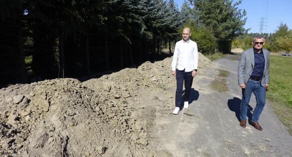  Burmistrz (po prawej) i Wiceburmistrz Drzewicy idą asfaltową drogą wzdłuż wykopu ziemnego i pasa iglastych drzew.