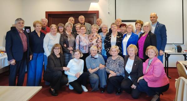 Pamiątkowe zdjęcie grupy uczestników i organizatorów spotkania rad seniorów, ustawionych w kilku rzędach w sali konferencyjnej. 